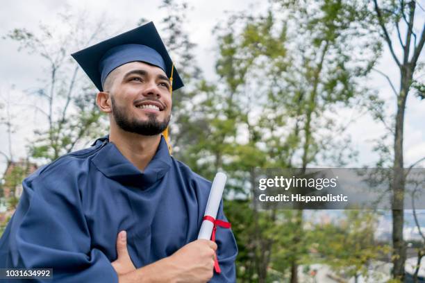 lateinamerikanische junger mann sehr glücklich nach seinem diplomabschluss wegschauen mit armen gekreuzt - high school graduation stock-fotos und bilder