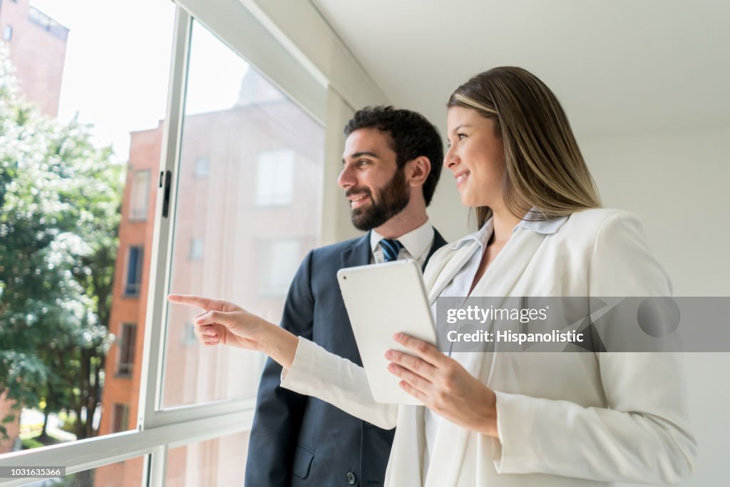 Beautiful real estate agent pointing at the view to customer both looking very happy