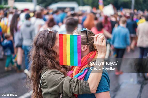 female couple hiding behind rainbow flag - march for marriage equality stock pictures, royalty-free photos & images