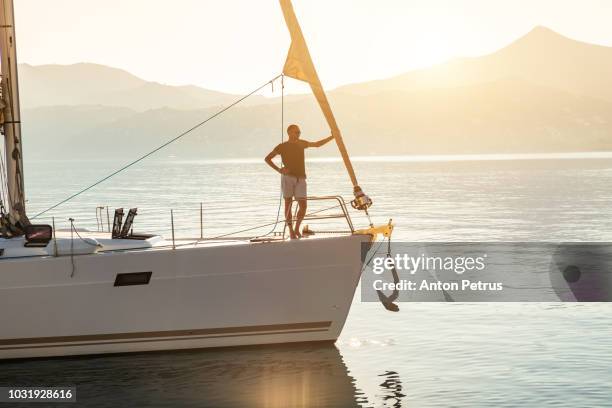 young guy on the bow of the yacht at sunset - luxury yacht stock pictures, royalty-free photos & images