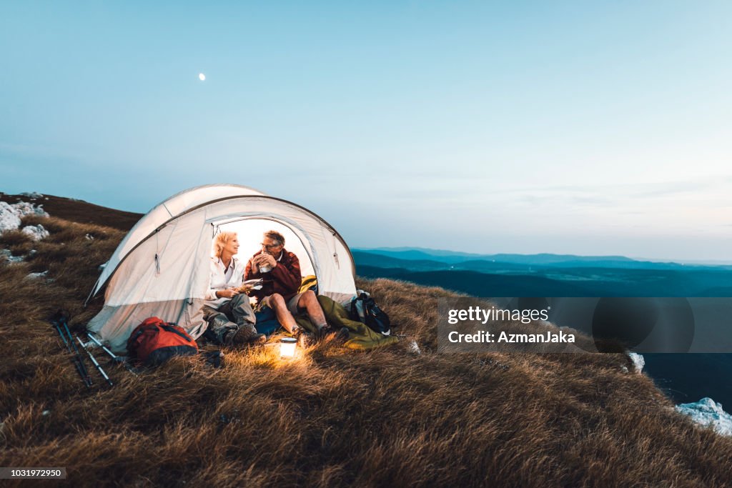 Senior pareja acampando en las montañas y comer un bocadillo