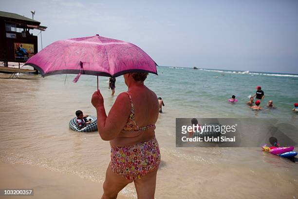 An Israeli woman holding an umbrella walks past Palestinian children from the West Bank village of Jahalin, as they spend the day at the beach on...