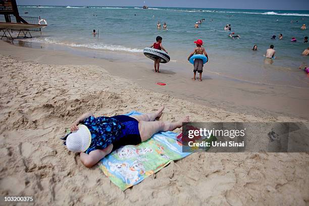 An Israeli woman lies on the sand as Palestinian children from the West Bank village of Jahalin enjoy a day in the beach, on August 2, 2010 in Bat...