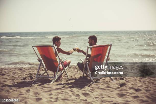 hombres bebiendo cerveza en la playa - man on the beach relaxing in deckchair fotografías e imágenes de stock