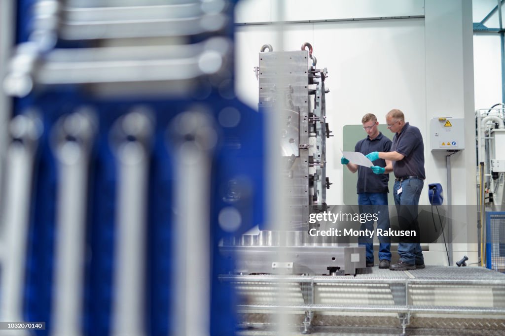 Engineer instructing apprentice on CNC machine in gearbox factory