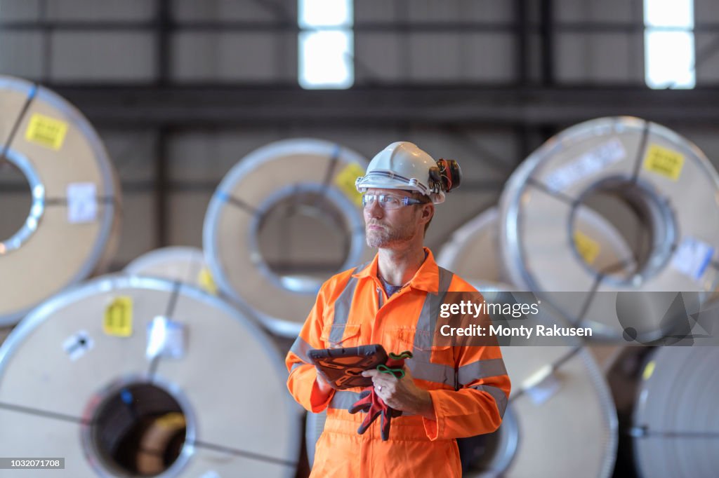 Portrait of worker using digital tablet by rows of sheet steel in storage at port