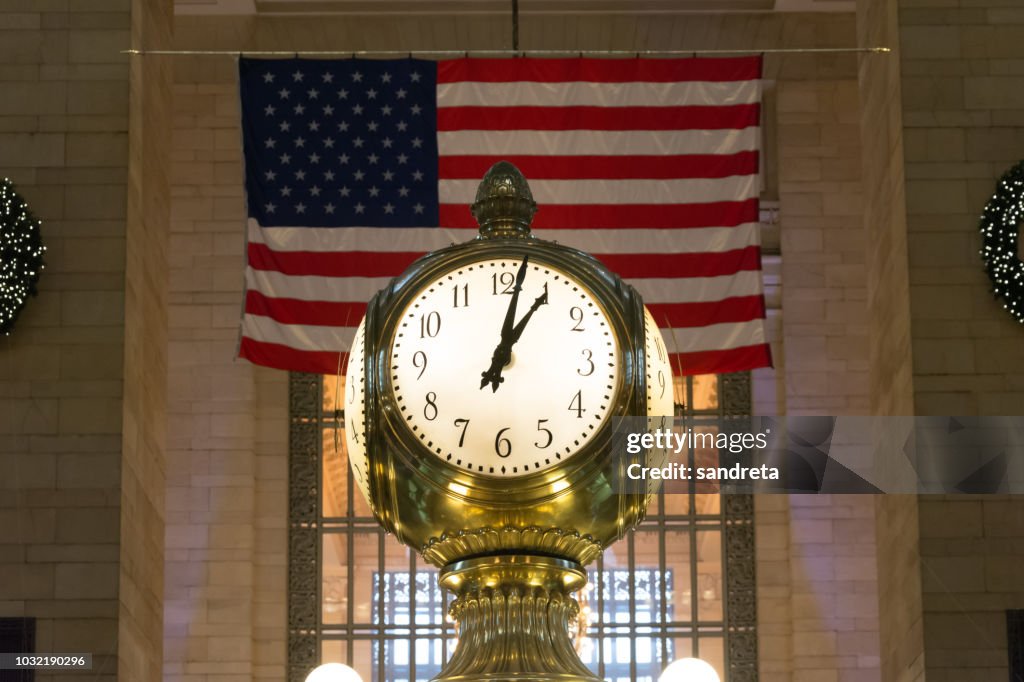 Primer plano del reloj de Grand Central, en Nueva York. Al fondo la bandera americana, y a los lados parte de la decoración navideña