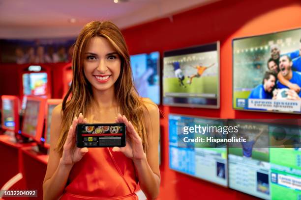 hermosa mujer de pie al lado de deportes en vivo mientras sostiene un smartphone mostrando sus apuestas de apuestas en el casino - turnover sport fotografías e imágenes de stock