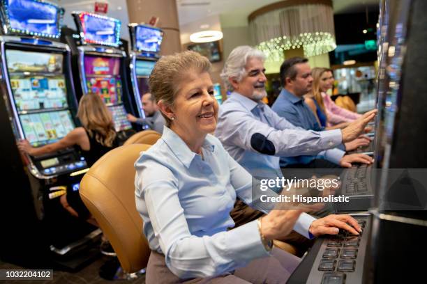 senior woman gambling on slot machine looking very happy - casino elegance stock pictures, royalty-free photos & images