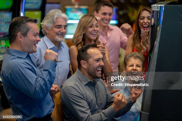 joyful latin american man celebrating he won jackpot on slot machine and people around him celebrating - old slot machine stock pictures, royalty-free photos & images