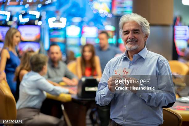 senior man at the casino holding a ten and an ace while looking at camera smiling - blackjack stock pictures, royalty-free photos & images