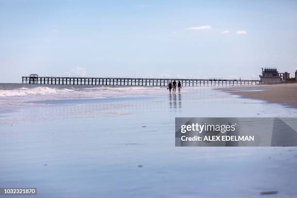 People walk on a nearly empty beach in Myrtle Beach, South Carolina on September 12, 2018. - Hurricane Florence was downgraded to a Category 3 storm...