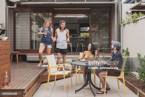 junges paar bringen lebensmittel an zwei freunde sitzen auf der terrasse - australian bbq stock-fotos und bilder