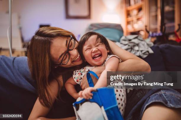 pretty young mom hugging and playing with baby on the sofa joyfully - asian baby fotografías e imágenes de stock