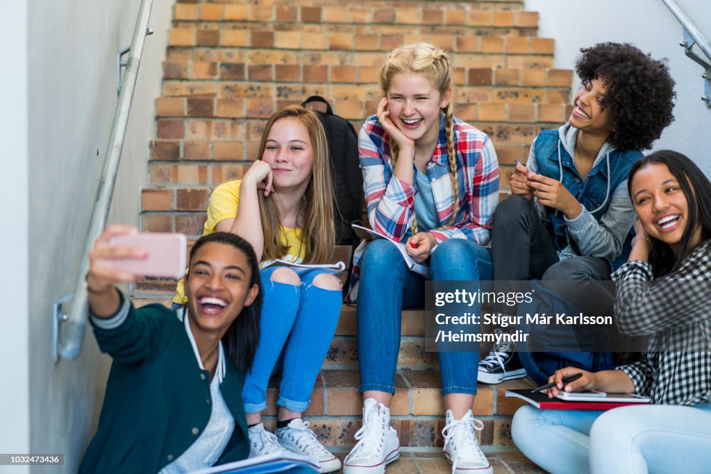 Happy students taking selfie on steps in school