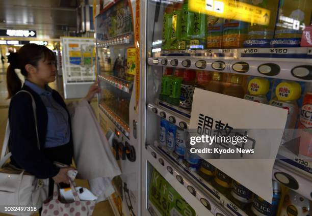 Woman buys a drink at JR Sapporo Station on Sept. 12 from a vending machine whose lights are turned off to save electricity amid continuing power...