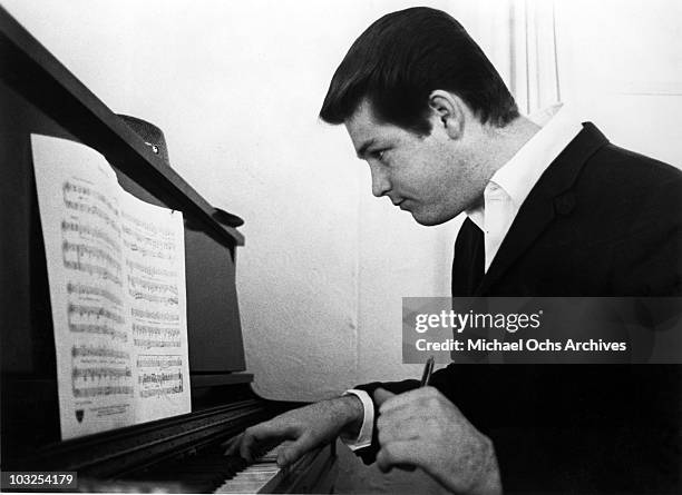 Musician Brian Wilson of the rock and roll band "The Beach Boys" works on a composition on an upright piano while reading music in 1964 in Los...