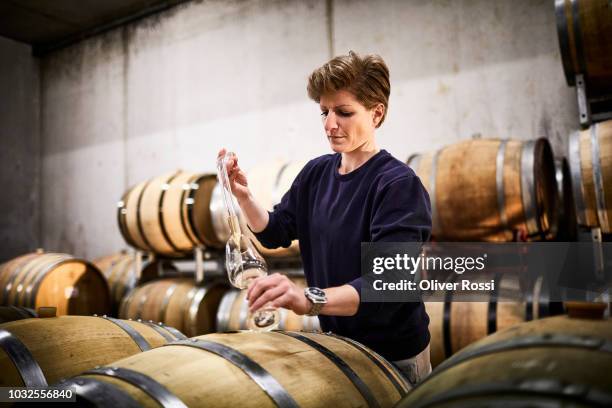 female vintner in wine cellar pouring wine into glass - viticulture fotografías e imágenes de stock