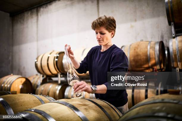 female vintner in wine cellar pouring wine into glass - wijnbouw stockfoto's en -beelden