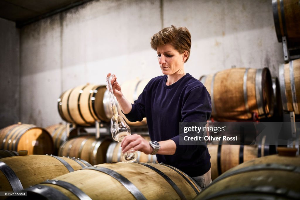 Female vintner in wine cellar pouring wine into glass