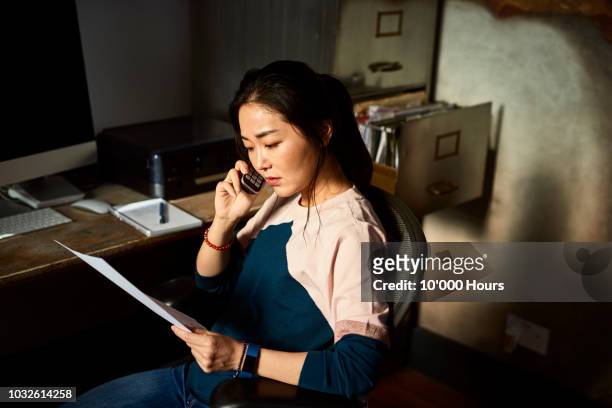 portrait of korean woman on cell phone reading important document - freelance work stock pictures, royalty-free photos & images