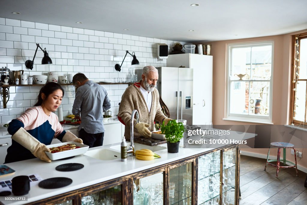 Woman placing hot lasagne dish on counter with father in law in kitchen