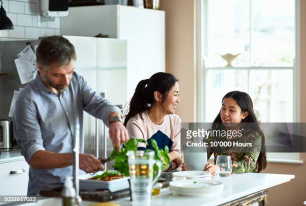 mother and daughter chatting in kitchen as father makes dinner - asian couple dinner stockfoto's en -beelden