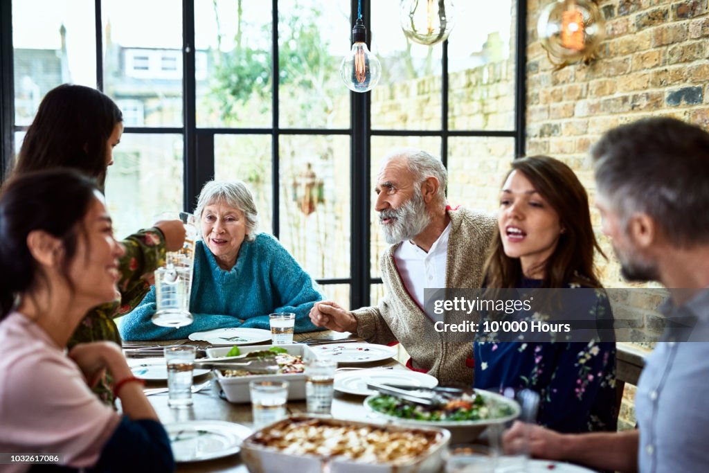 Extended family sitting round dinner table chatting and eating dinner