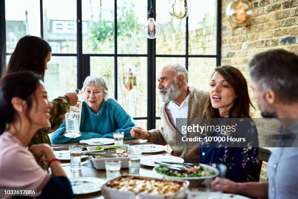 extended family sitting round dinner table chatting and eating dinner - family at dining table stock pictures, royalty-free photos & images