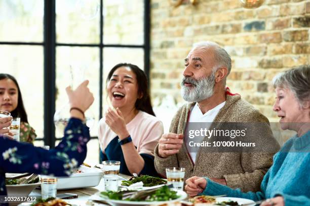 cheerful mature man telling story over dinner with family laughing - seniors and group and diverse foto e immagini stock