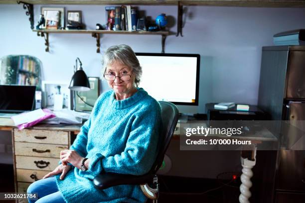 cheerful senior woman sitting at desk and smiling towards camera - author stock-fotos und bilder