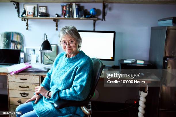 cheerful senior woman sitting at desk and smiling towards camera - female authors stock pictures, royalty-free photos & images