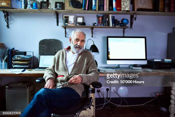 mature man sitting in home office looking at camera - authors fotografías e imágenes de stock