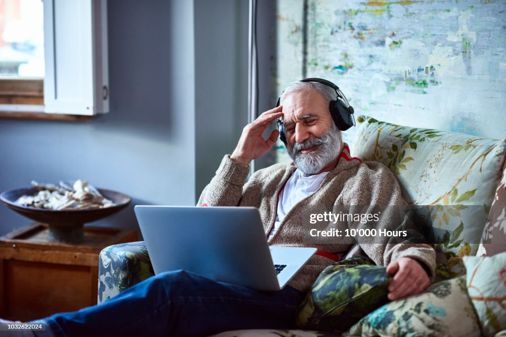 Portrait of mature man streaming movie on laptop wearing headphones