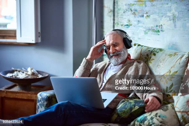 portrait of mature man streaming movie on laptop wearing headphones - mood stream stock pictures, royalty-free photos & images