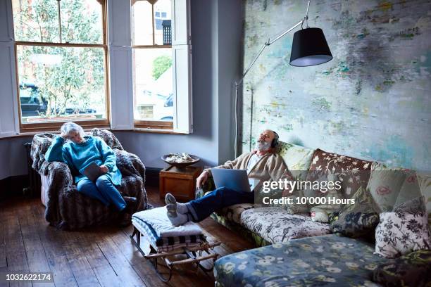 boho couple relaxing at home on sofa with music and ebook - sofa chair stock pictures, royalty-free photos & images