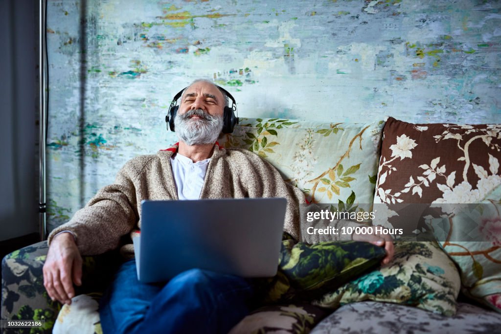 Portrait of mature man on sofa smiling and wearing headphones