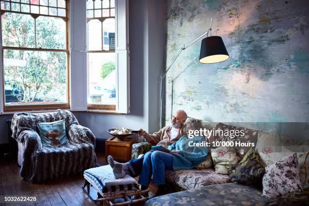 senior couple relaxing on sofa in boho living room watching tv - shared living room stock pictures, royalty-free photos & images