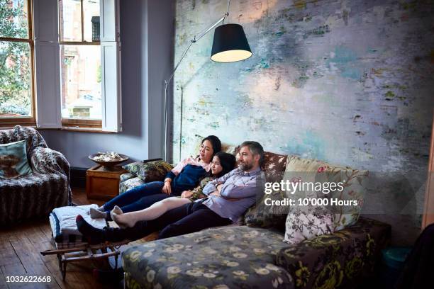 family watching television together at home on sofa - men women & children film stock-fotos und bilder