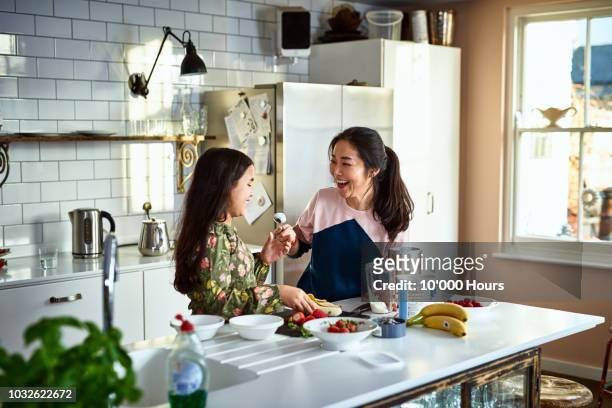 mother teasing daughter in kitchen whilst making smoothies - family at kitchen stockfoto's en -beelden