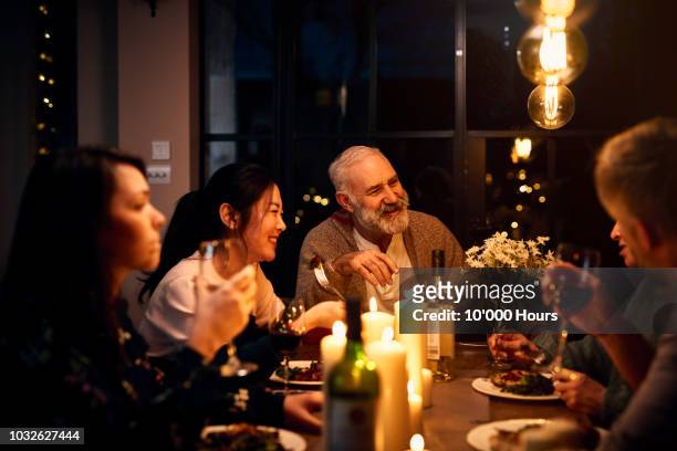 cheerful guests at dinner table listening to friend and drinking wine - happy family eating photos et images de collection