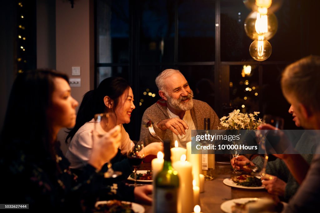 Cheerful guests at dinner table listening to friend and drinking wine