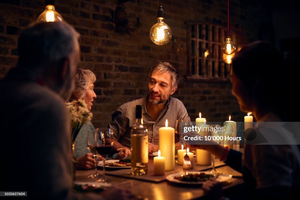 Mature man talking to friends at candlelit dinner table