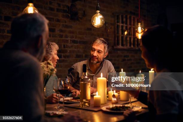 mature man talking to friends at candlelit dinner table - cozy friends stock pictures, royalty-free photos & images