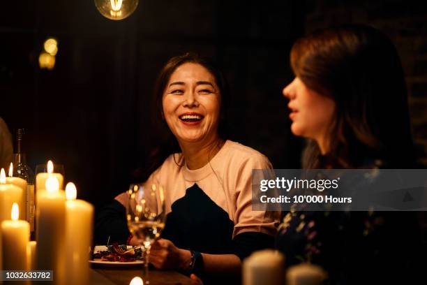 joyful korean woman in her 30s laughing with friend over dinner - dinner party at home stockfoto's en -beelden