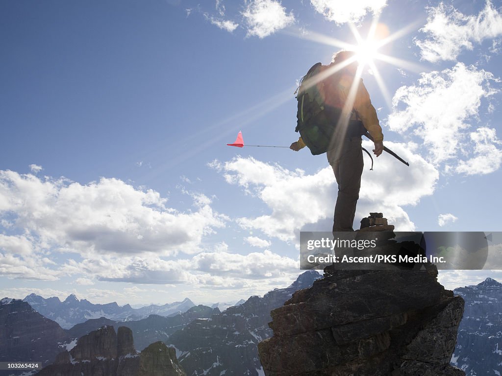 Mountaineer stands on mtn summit, holds flag