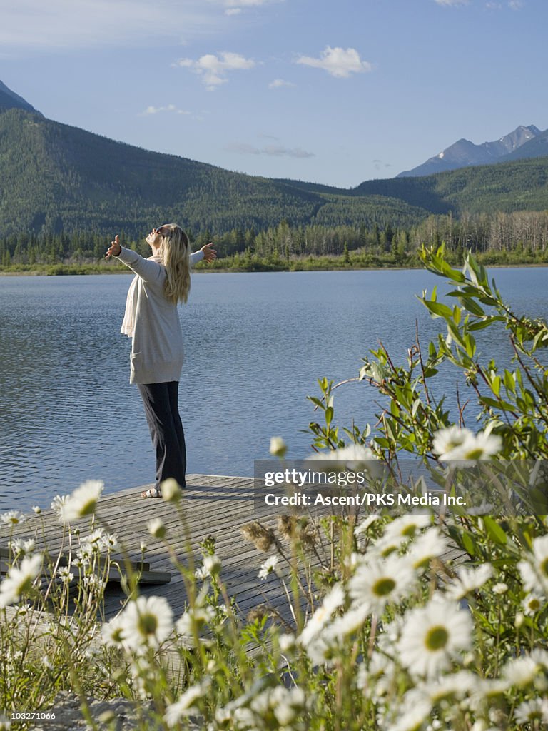 Woman stretches arms on mountain lake wharf