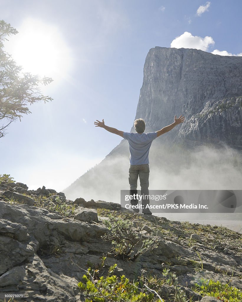 Man stands on mtn knoll in mist, arms stretched