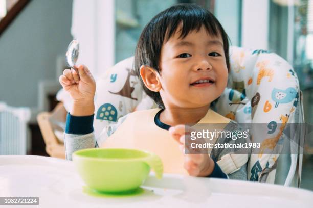 asian baby boy feeding himself on high chair. - asian spoon feeding stock pictures, royalty-free photos & images