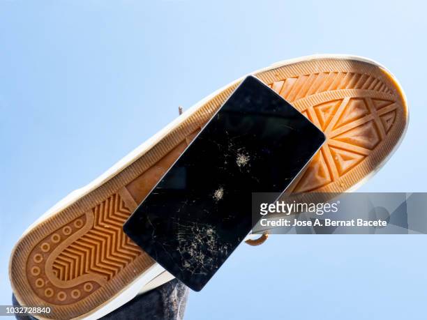 slipper of white color of a person squishing a mobile phone against the soil, outdoors. - distruzione foto e immagini stock